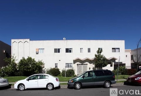 A white car is parked in front of a white building with a green car parked behind it.