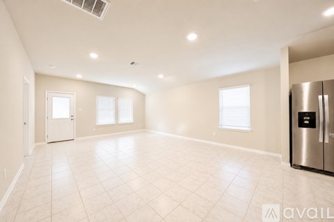 A spacious, empty room with a stainless steel refrigerator on the right side.