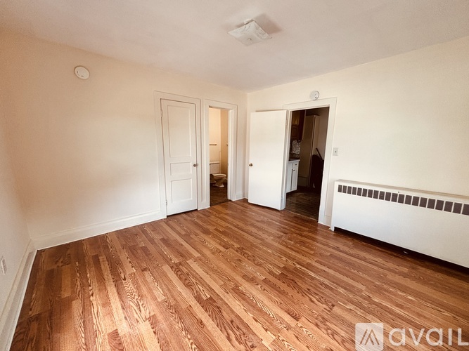 A room with wooden flooring and white walls, with two doors and a window.