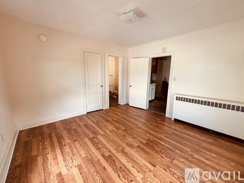 A room with wooden flooring and white walls, with two doors and a window.