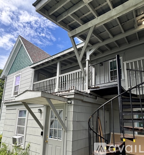 A house with a grey siding and a green roof with a balcony and a staircase.