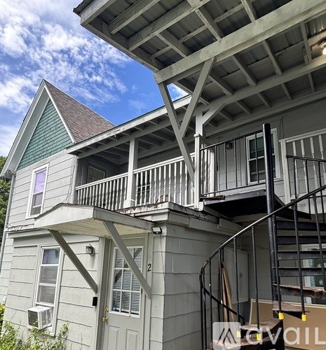 A house with a grey siding and a green roof with a balcony and a staircase.