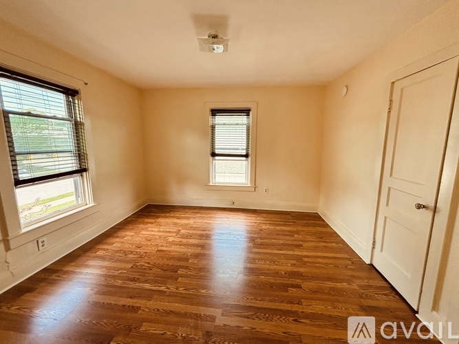 A room with wooden flooring and two windows.
