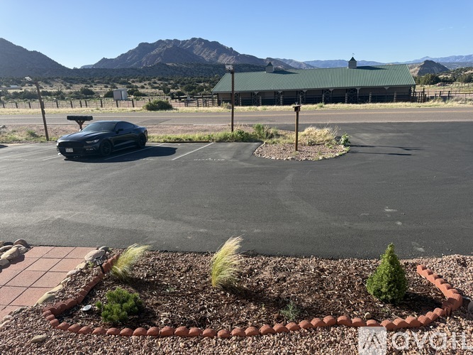 A black car is parked in a parking lot with a green building in the background.