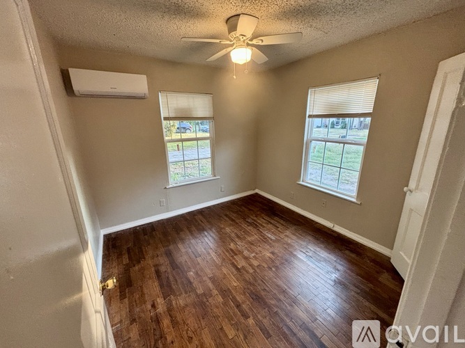A room with wooden flooring and two windows.