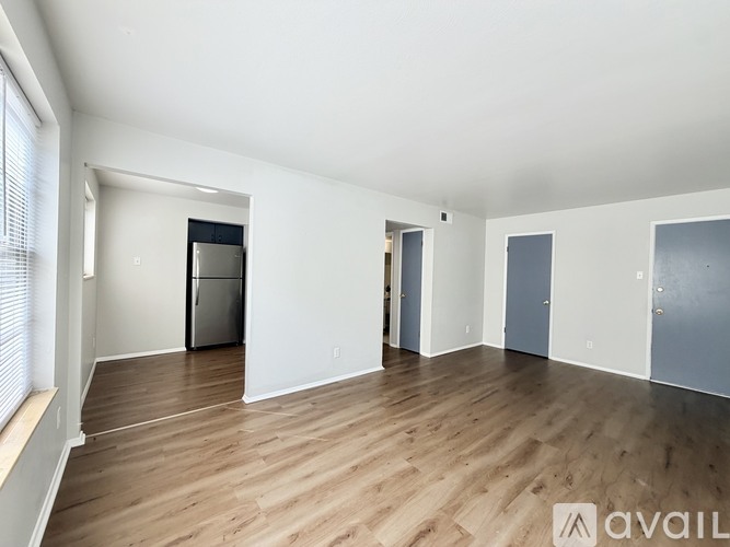 A spacious empty room with wooden flooring and white walls.