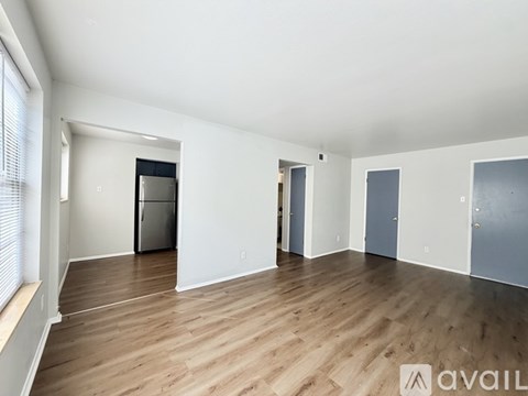 A spacious empty room with wooden flooring and white walls.