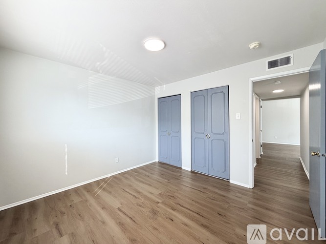 A room with wooden flooring and white walls, with a door on the right and a window on the left.