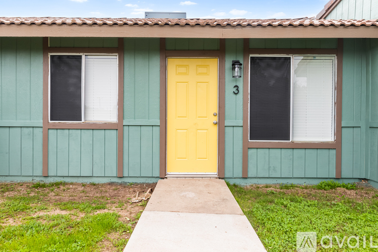 A house with a yellow door and two windows with white curtains.