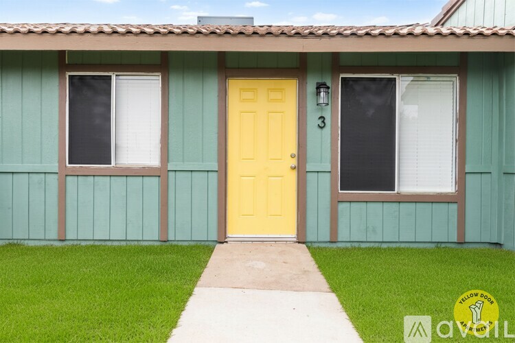 A house with a yellow door and two windows with white curtains.