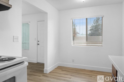 A white kitchen with a stove top oven and a window with blinds.
