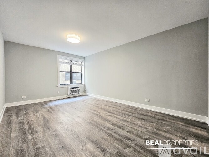 A spacious room with wooden flooring and a window with blinds.