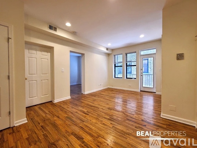 A spacious room with wooden floors and white walls, with a door leading to another room visible in the background.