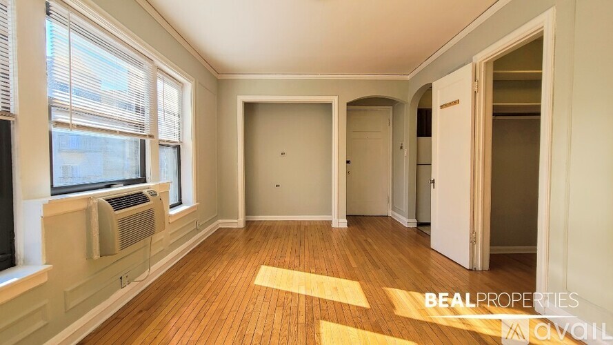 A room with wooden floors and white walls, with a window on the left and a door on the right.