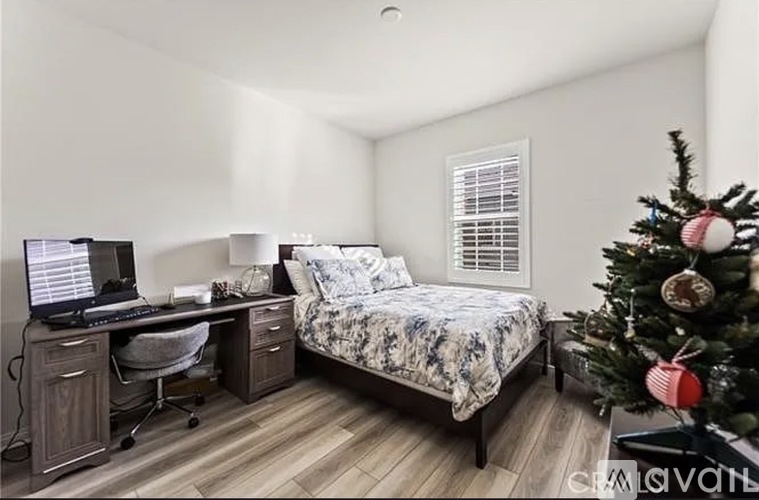 A bedroom with a bed, desk, and chair, decorated with a Christmas tree.