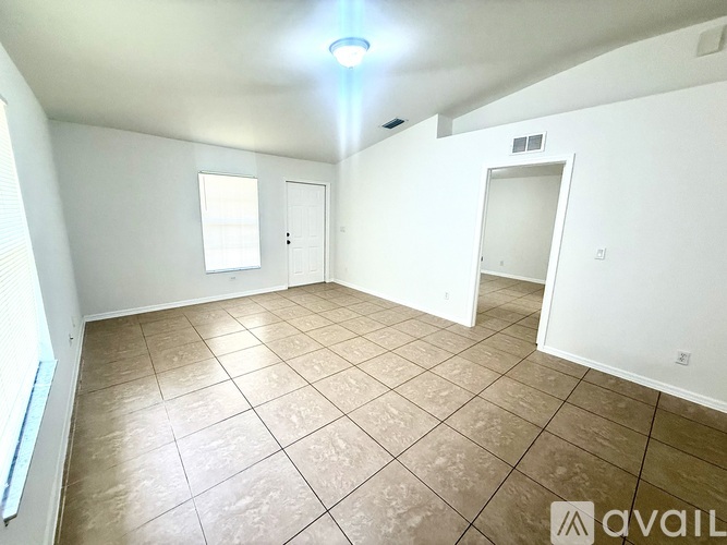 A room with tiled flooring and white walls, with a window on the left and a door on the right.