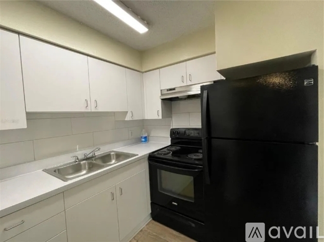 A black refrigerator is in a kitchen with white cabinets.