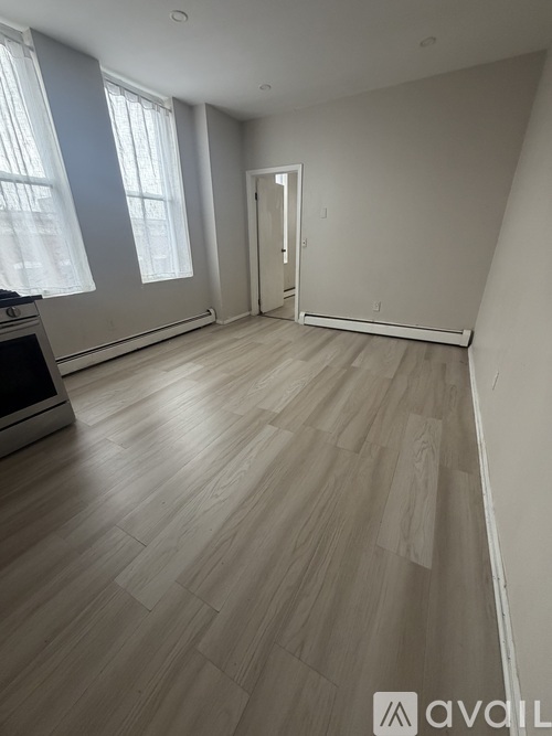 A spacious room with light wood flooring and a large window.
