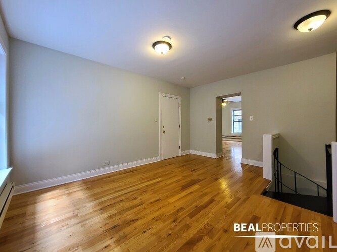 A spacious room with wooden floors and white walls, with a staircase on the right side.