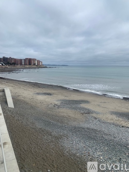 A beach with a cloudy sky and buildings in the distance.