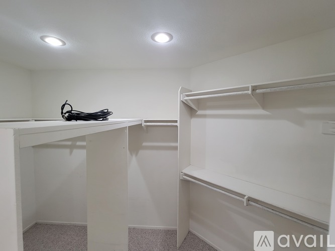 A small, white, and empty bedroom with a single bed and a desk.