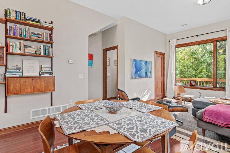 A dining room with a table surrounded by chairs and a bookshelf filled with books.