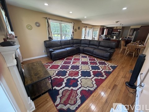 A living room with a black leather couch and a rug.