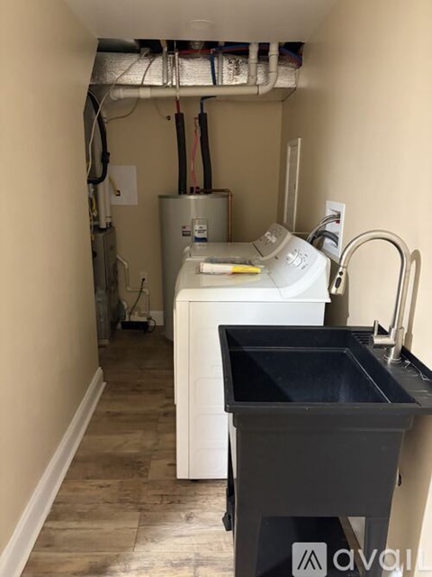 A kitchen sink with a white dishwasher and a silver refrigerator in a narrow hallway.