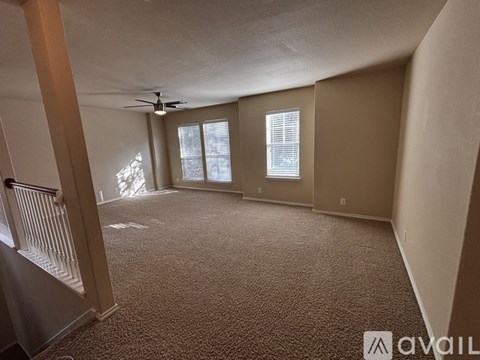 A carpeted room with a ceiling fan and two windows.