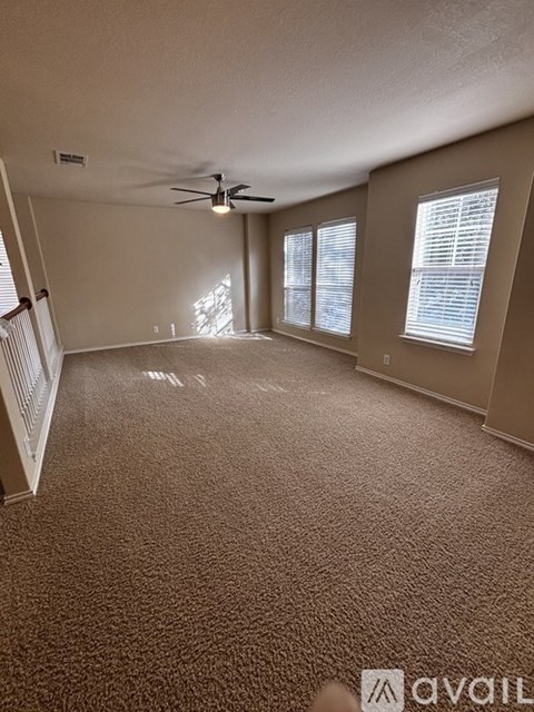 A carpeted room with a ceiling fan and three windows.