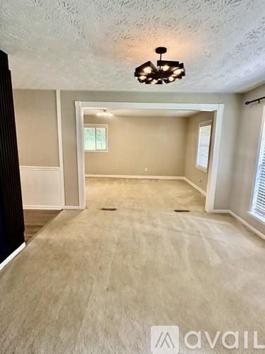 A spacious room with a carpeted floor and a chandelier hanging from the ceiling.