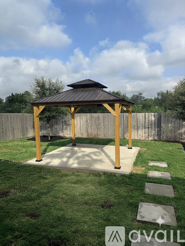 A wooden gazebo with a black roof is situated in a grassy area with a stone pathway leading to it.