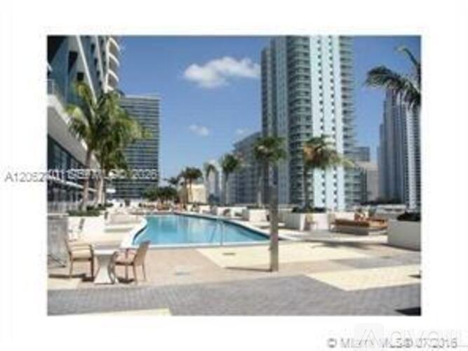 A pool area with chairs and palm trees in front of apartment buildings.