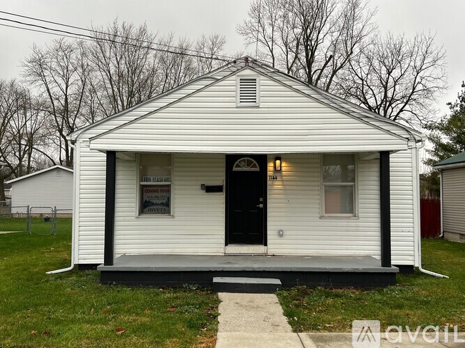 A small white house with a black door and a sign on the window.