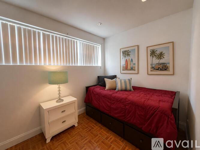 A bedroom with a red bed, a white nightstand with a lamp, and two framed pictures on the wall.