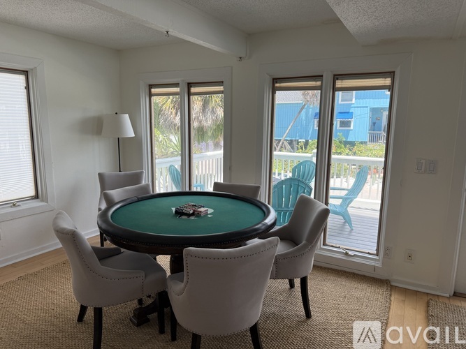 A poker table surrounded by chairs in a room with a view of a pool and a blue building.