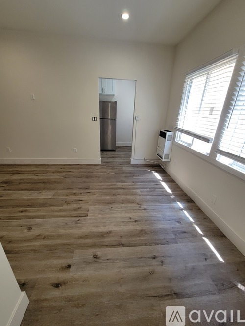 A room with wooden flooring and a refrigerator in the background.