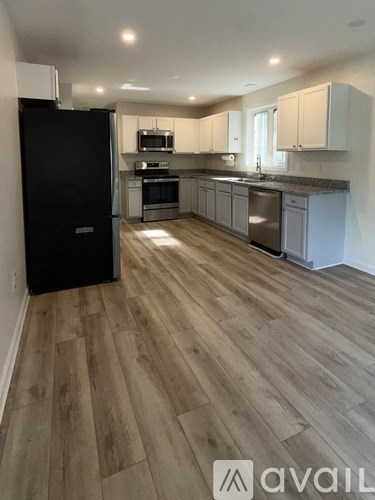 A kitchen with a black fridge and wooden flooring.