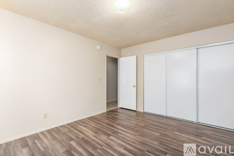 A room with wooden flooring and white walls, featuring a sliding door and a closet with a mirror.