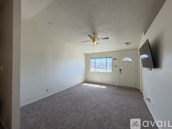 A spacious room with a ceiling fan and a flat-screen TV mounted on the wall.