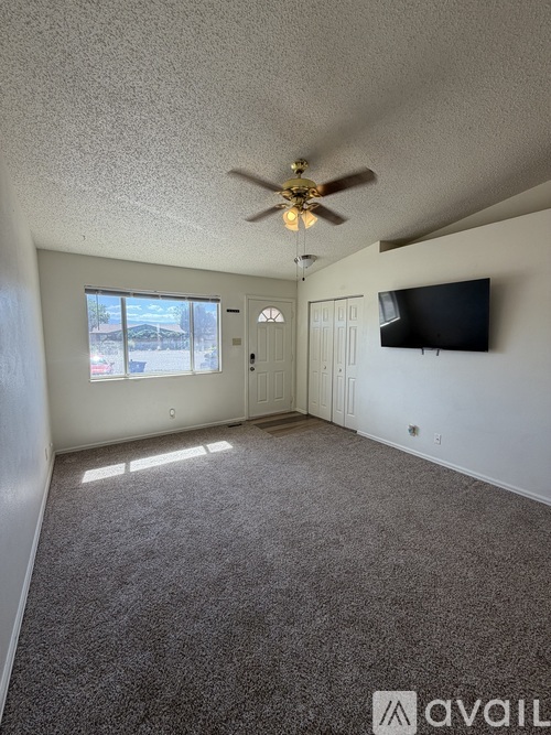 A living room with a ceiling fan and a flat screen TV mounted on the wall.