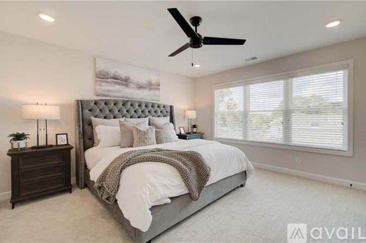 A bedroom with a large bed, a ceiling fan, and a window with blinds.