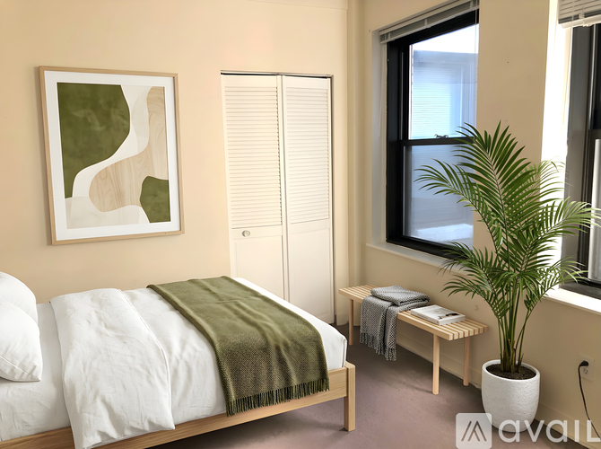 A bedroom with a bed, a bench, a plant, and a painting on the wall.