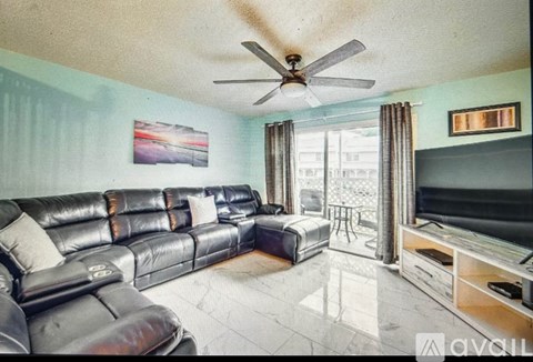 A living room with a black leather couch and a ceiling fan.