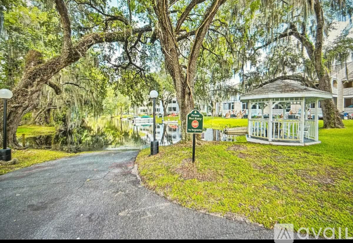 A tree-lined pathway leads to a gazebo in a park.