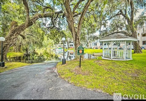 A tree-lined pathway leads to a gazebo in a park.