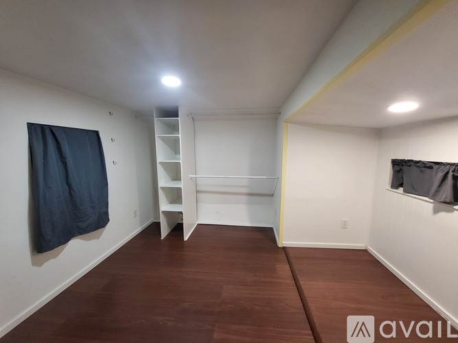 A room with a wooden floor and a white wall with a coat hanging on it.