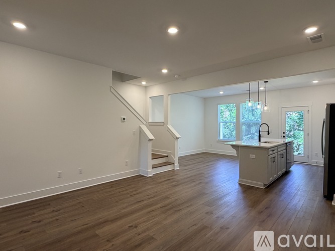A spacious room with wooden floors and a staircase leading to the upper level.