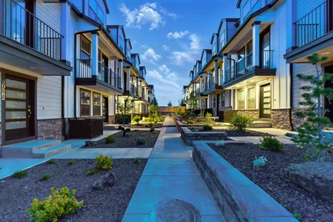 A row of modern townhouses with a sidewalk in front.