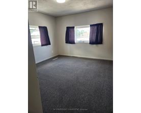 A room with grey carpet and two windows with purple curtains.